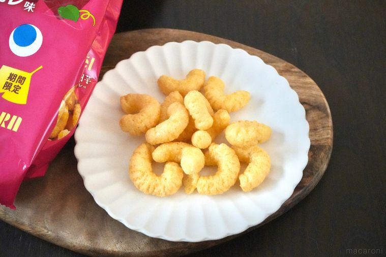 木のカッティングボードと白い皿にのった安納芋ブリュレ味のコーンスナックとピンク色のパッケージ