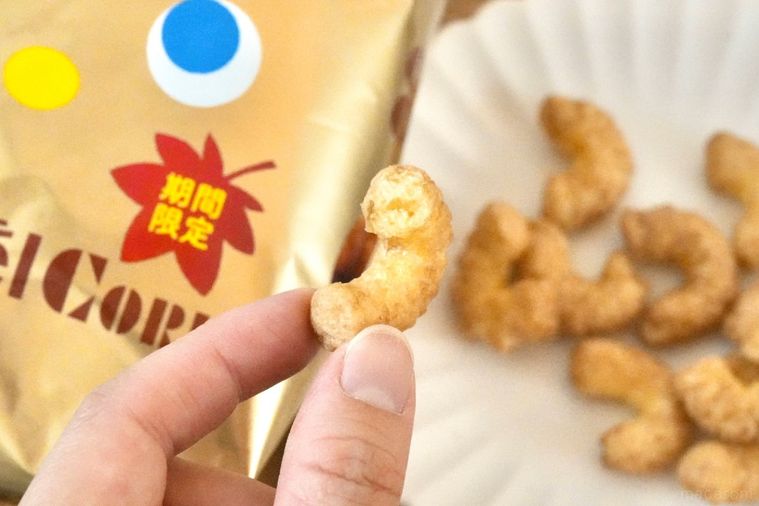 木のカッティングボードと白い皿にのった和栗モンブラン味のコーンスナックを持つ手と金色のパッケージ