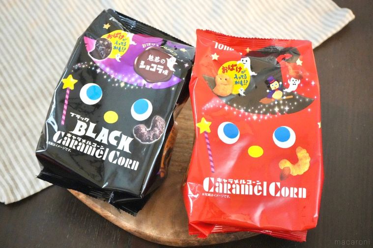 木のカッティングボードにのった黒と赤色のハロウィンパッケージのコーンスナック菓子とストライプの布