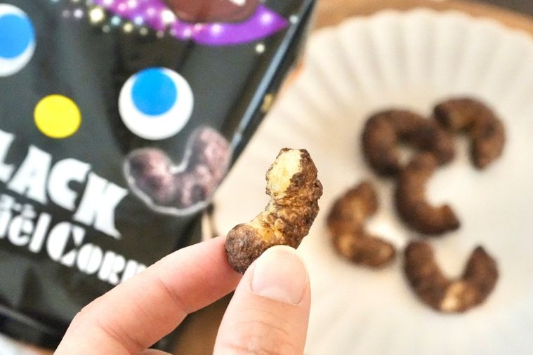 木のカッティングボードと白い皿にのった黒いコーンスナックを手に持つ様子と黒いハロウィンパッケージ