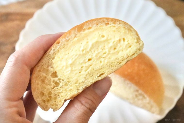 木のカッティングボードと白い皿にのったカスタードホイップ冷やしクリームパンを手に持つ様子