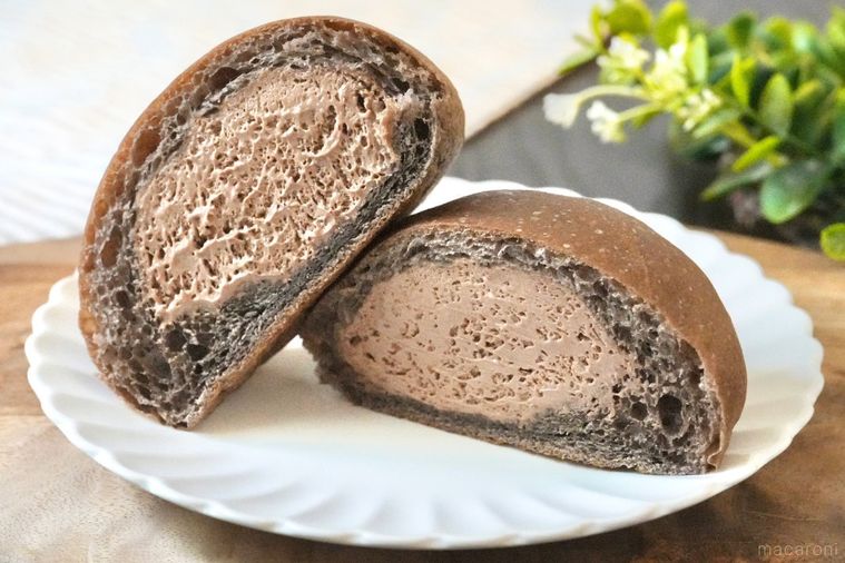 木のカッティングボードと白い皿にのったチョコレートホイップクリーム入りの丸いクリームパンの断面とストライプの布とグリーン