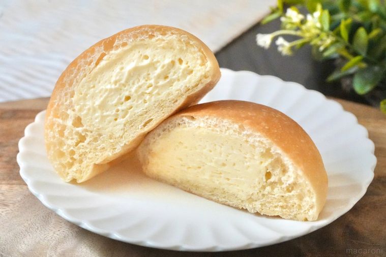 木のカッティングボードと白い皿にのった丸いクリームパンの断面とストライプの布とグリーン