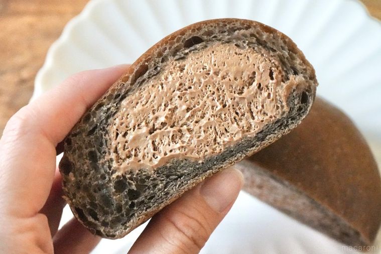 木のカッティングボードと白い皿にのったチョコレートホイップクリーム入りの丸いクリームパンを手に持つ様子