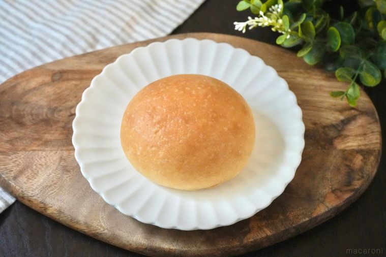 木のカッティングボードと白い皿にのった丸いクリームパンとストライプの布とグリーン