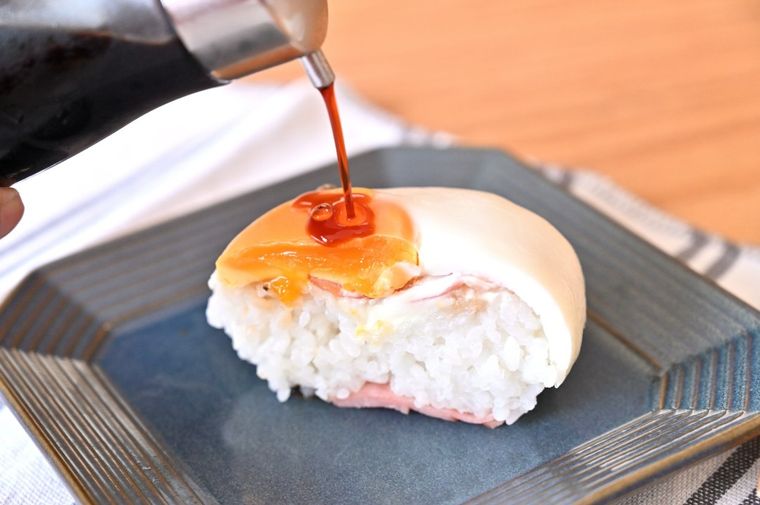 炙りベーコンエッグおにぎりにしょうゆをたらしている