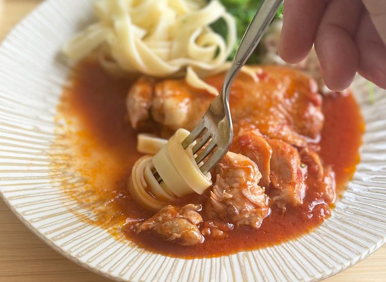 チキンのトマト煮のソースにパスタを絡めている写真