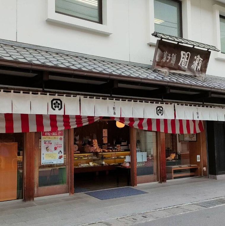 木の看板や白いのれんがかかった菓子舗 間瀬 本店の外観