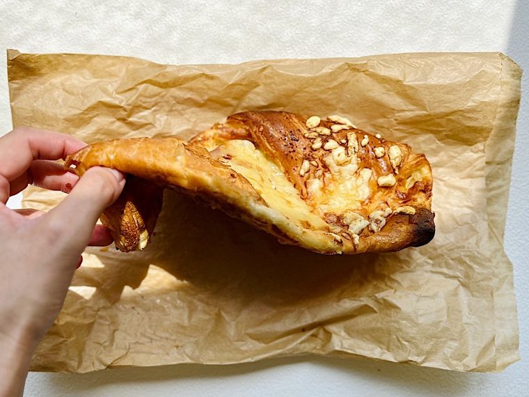 袋の上に置いたコストコ フードコートのクロワッサンハムチーズを手で持ち上げているところ