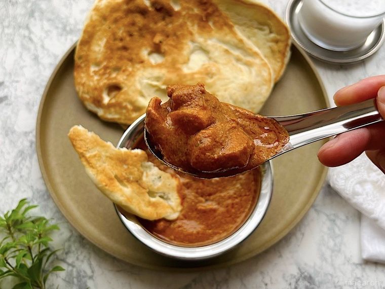 ひと口分スプーンですくったコストコのバターチキンカレー、ちぎってカレーに浸したナン、グラスに入ったドリンク