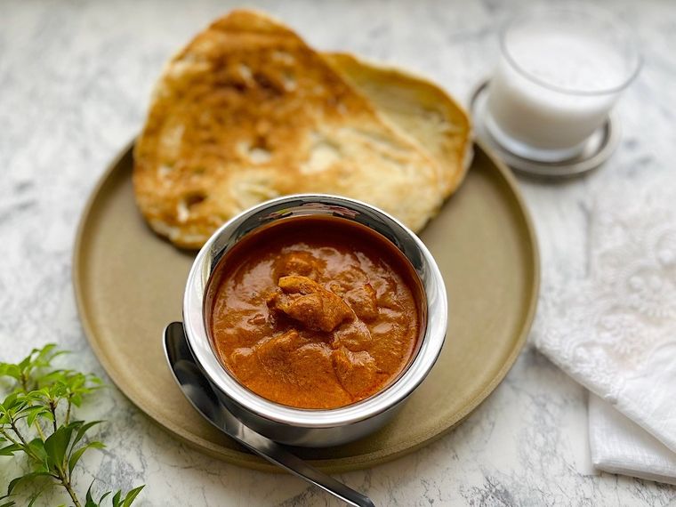 プレートの上に盛り付けたコストコのバターチキンカレーとグラスに入ったドリンク、白いナプキン