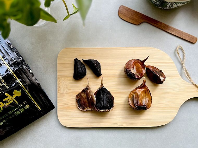 ウッドボードに並べた薄皮がついたままのコストコの黒にんにくと薄皮をむいた黒にんにく、木製バターナイフ