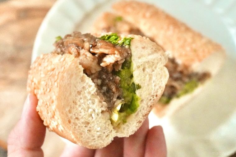 木のカッティングボードと白い皿にのった牛カルビサンドイッチの断面を手で持つ様子