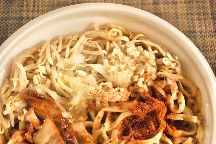 白い容器に盛られたコンビニの旨辛二郎系ラーメンの具材のアップと赤いスパイス調味料