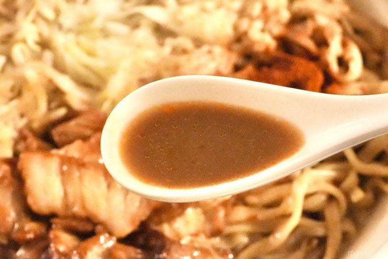 もやしとキャベツとにんにくがのったコンビニの旨辛二郎系ラーメンのスープを白いレンゲですくう様子
