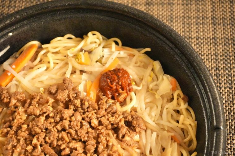 黒い容器に盛られたコンビニの豚そぼろのせにんにく焼きそばにのった辛味調味料