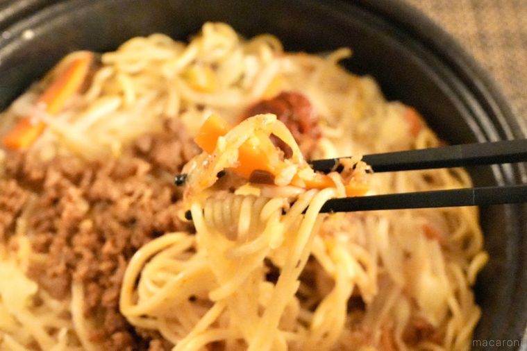 コンビニの豚そぼろのせにんにく焼きそばと野菜を黒い箸で持ち上げる様子
