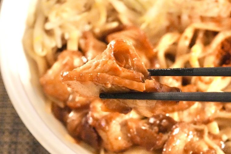 白い容器に盛られたコンビニの旨辛二郎系ラーメンのチャーシューを黒い箸で持ち上げる様子