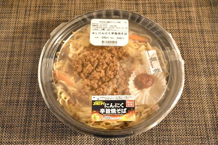 茶色いテーブルクロスとコンビニのにんにく焼きそばが入った黒い容器
