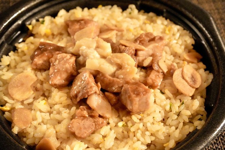 茶色いランチョンマットにのった黒い容器入りの背脂にんにく豚チャーハンのアップ