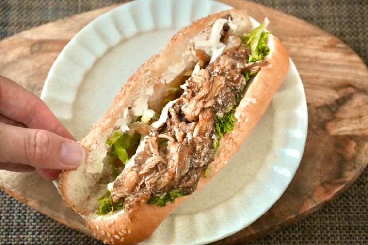 木のカッティングボードと白い皿にのった牛カルビサンドイッチを手で開く様子