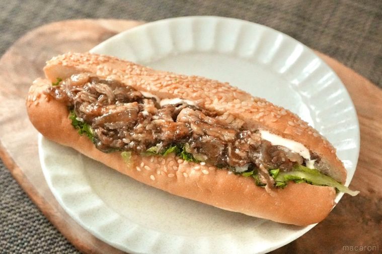 茶色いランチョンマットと木のカッティングボードと白い皿にのった野菜入り牛カルビサンドイッチ