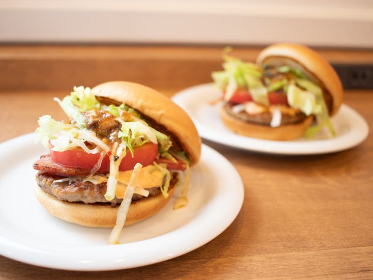 お皿にのったモスバーガー黒アヒージョ ベーコンバーガーが木製のカウンターの上に2個並んでいる