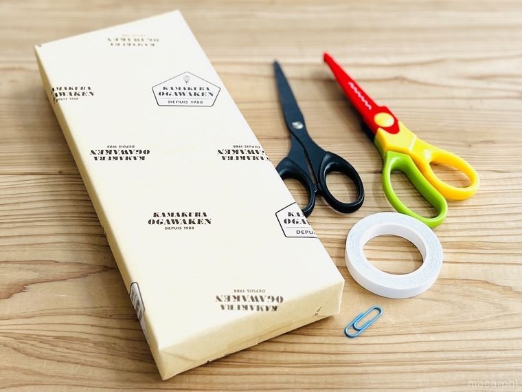 テーブルの上に包装紙で包まれたお菓子、はさみ、ピンキングはさみ、両面テープ、ゼムクリップが並んでいる