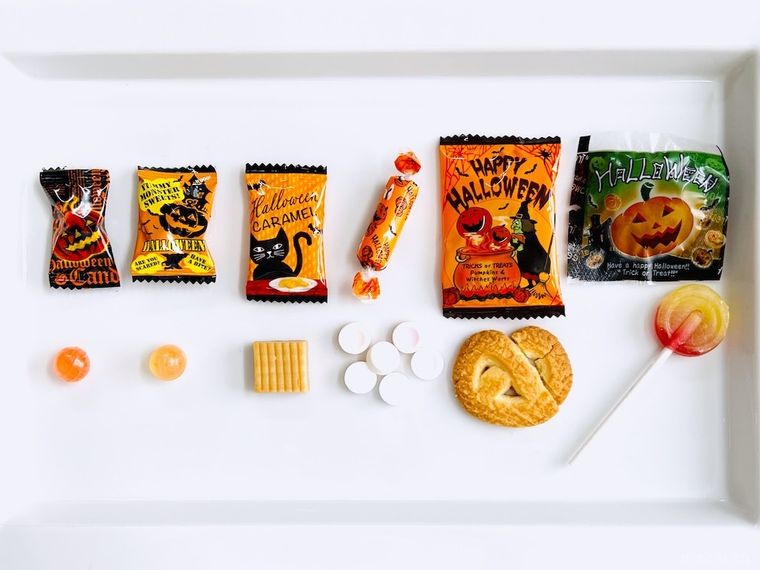 ハロウィン柄のパッケージに入ったロリーポップ、キャンディ、ラムネ、クッキー、キャラメルを袋から出した様子