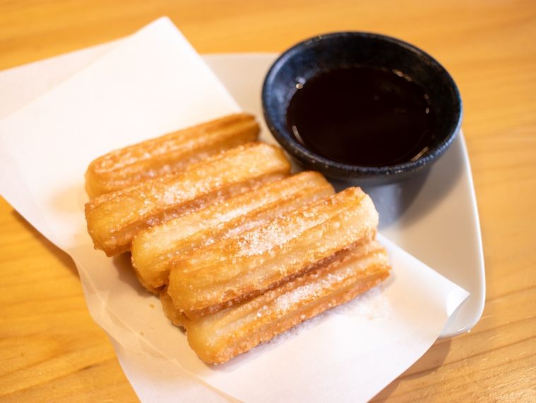 木製のテーブルに置かれた鳥貴族のメイプルシュガーチュロホットチョコソース添え