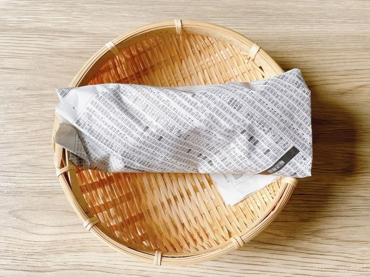 新聞紙で包んださつまいもをザルにおいたもの