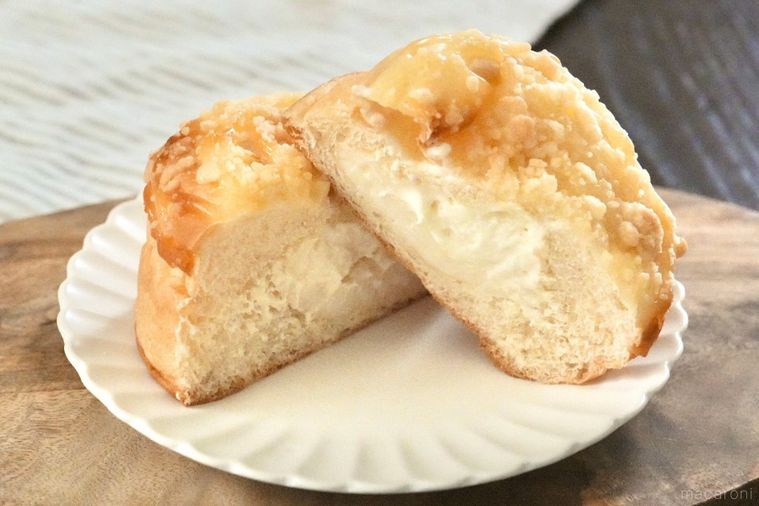 木のカッティングボードと白い皿にのったチーズクリームがトッピングされた菓子パンの断面とストライプの布