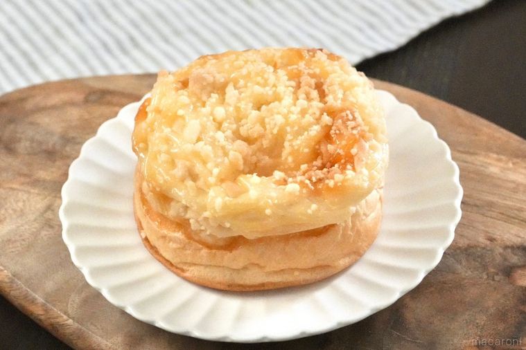 木のカッティングボードと白い皿にのったチーズクリームがトッピングされた菓子パンとストライプの布