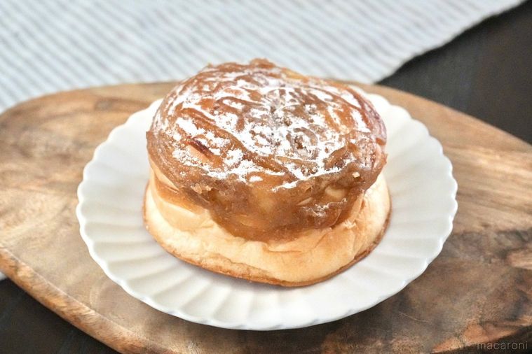 木のカッティングボードと白い皿にのったマロンクリームがトッピングされた菓子パンとストライプの布