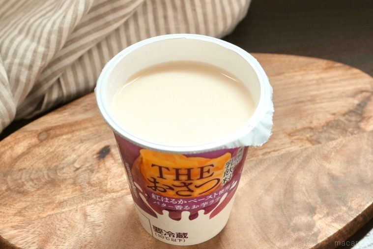 木のカッティングボードにのった紫色のパッケージのさつまいもドリンクのフタを開けた状態とストライプの布