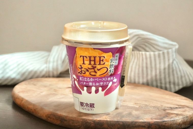 木のカッティングボードにのった紫色のパッケージのさつまいもドリンクとストライプの布