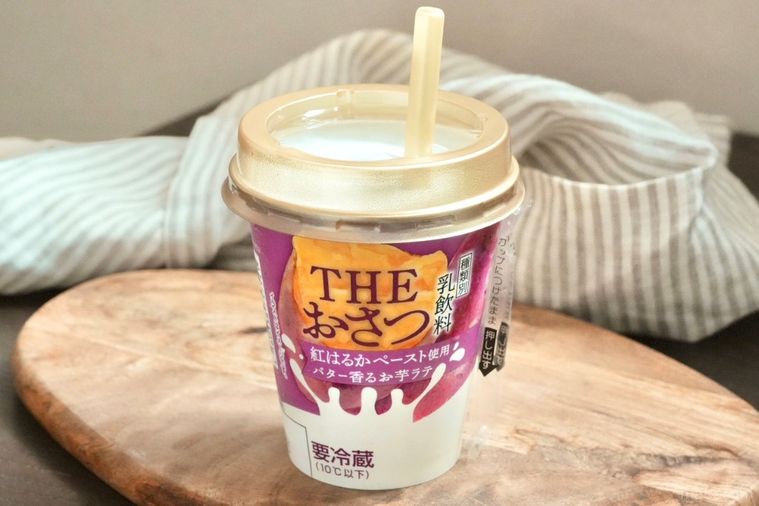 木のカッティングボードにのった紫色のパッケージのさつまいもドリンクとストライプの布