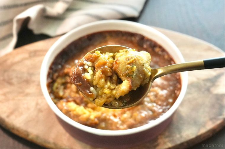 木のカッティングボードにのったコンビニの焼きカレーを金色と黒色のスプーンですくう様子