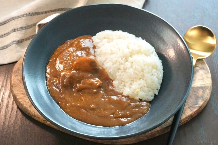 木のカッティングボードと黒い器にのったレトルトカレーと金色と黒色のスプーン