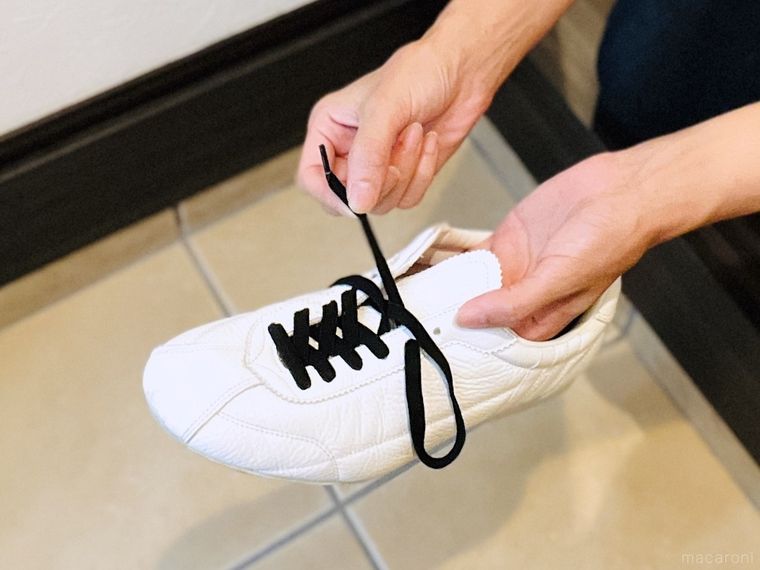 白いスニーカーの紐穴に黒い靴紐を通している様子