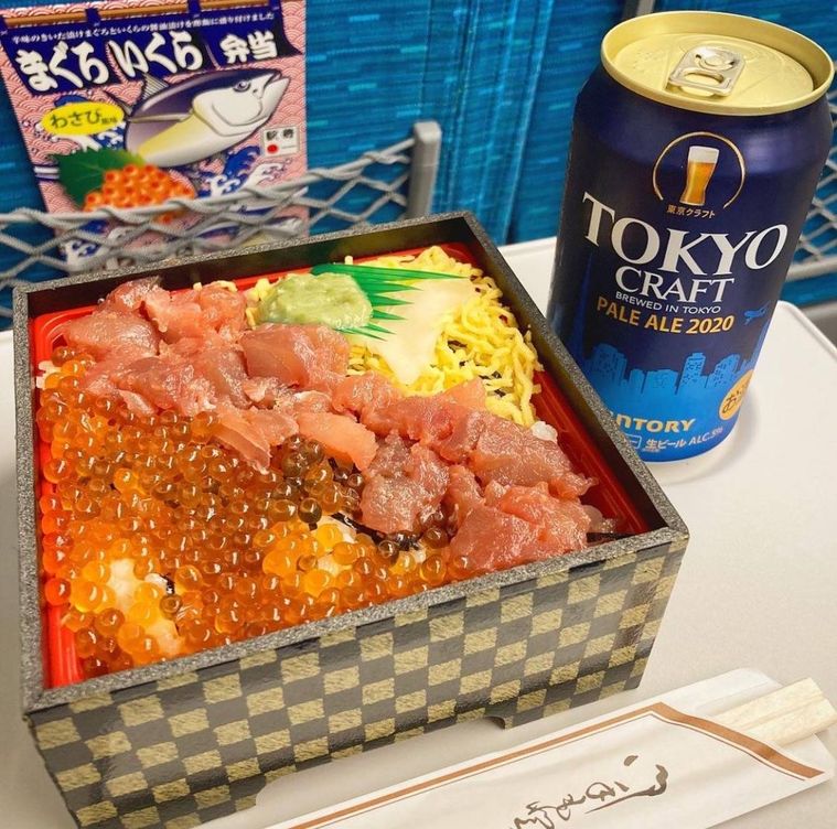 新幹線のテーブルに置かれたまぐろいくら弁当とビール