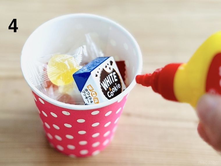 お菓子が入った紙コップのフチにボンドを塗っている様子