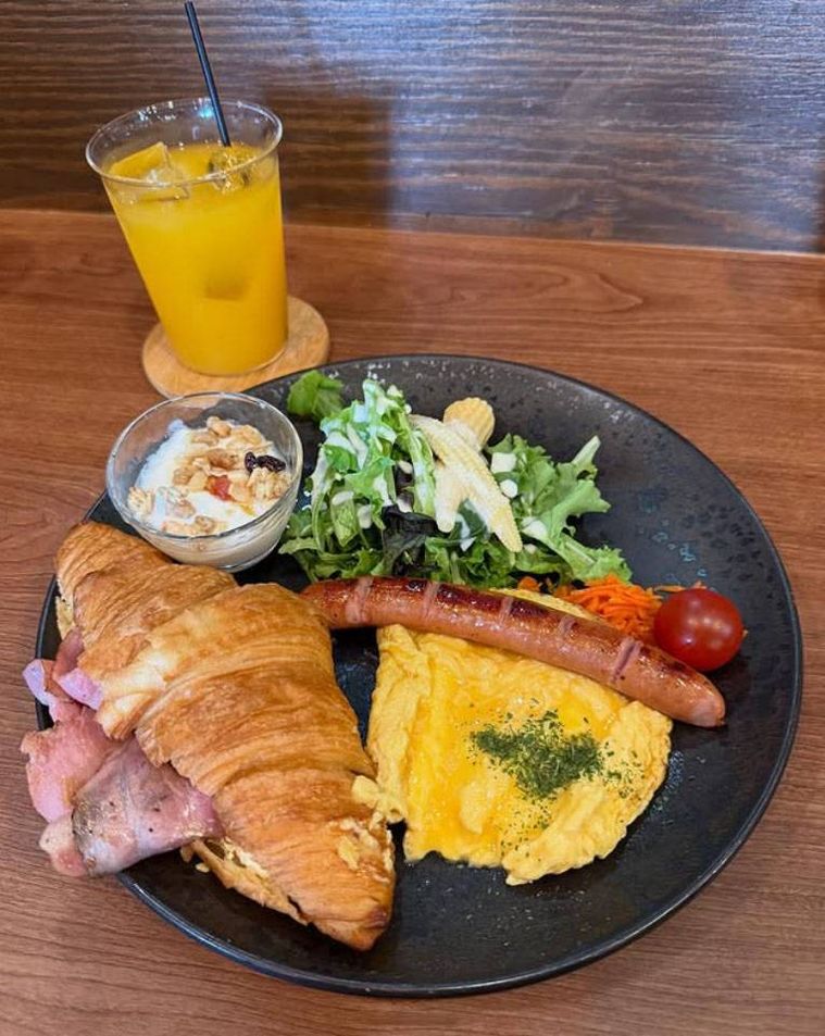 黒いプレートに盛られたベーコンエッグクロワッサンとオレンジジュース