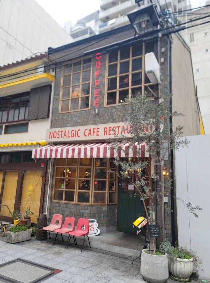 レンガ調の外壁に赤と白の日よけがかかったカフェ トキオナの外観