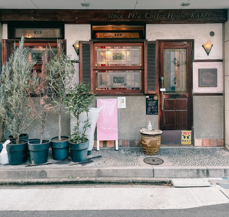 植木が置かれ、白やグレーの壁、木の扉と出窓のある外観