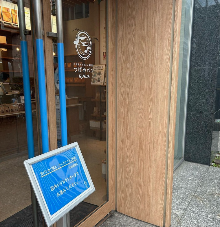 青い案内板、ガラス張り。扉にお店のロゴが白く入った外観