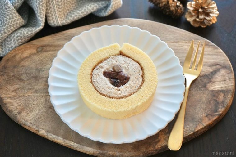 木のカッティングボードと白い皿にのった渋皮栗のプレミアムロールケーキと金のフォークとグレーの布