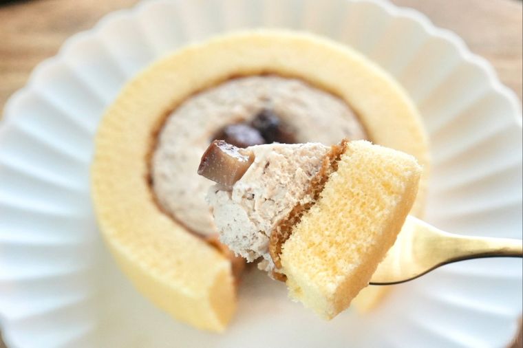 木のカッティングボードと白い皿にのった渋皮栗のプレミアムロールケーキを金のフォークで食べる様子