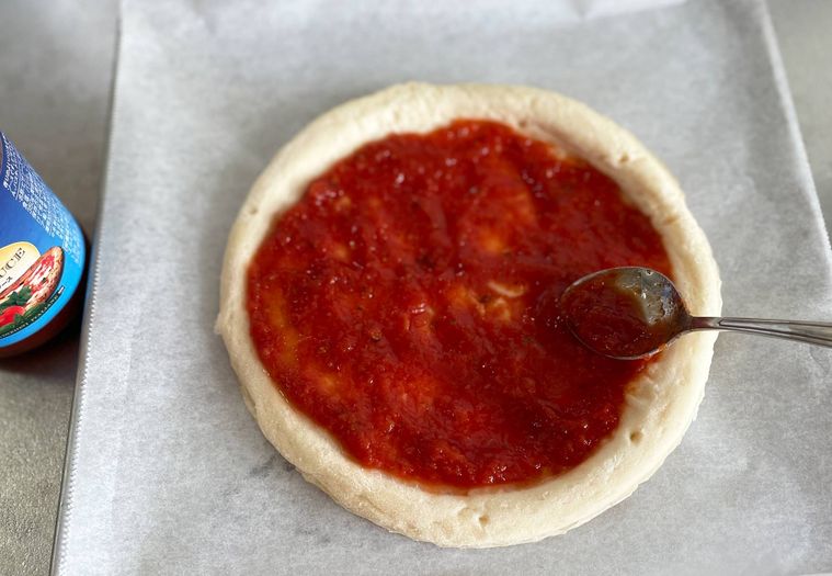 ピザクラフトにスプーンでピザソースを塗っている