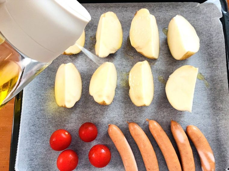 天板に並べたじゃがいも、トマト、ウィンナーに油をスプレーしている
